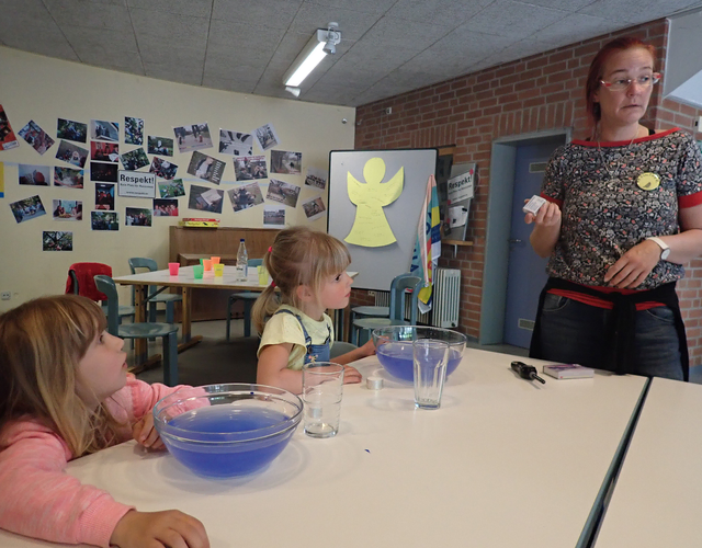 Frau erklärt Kindern ein Experiment mit Schüsseln voller blauer Flüssigkeit.