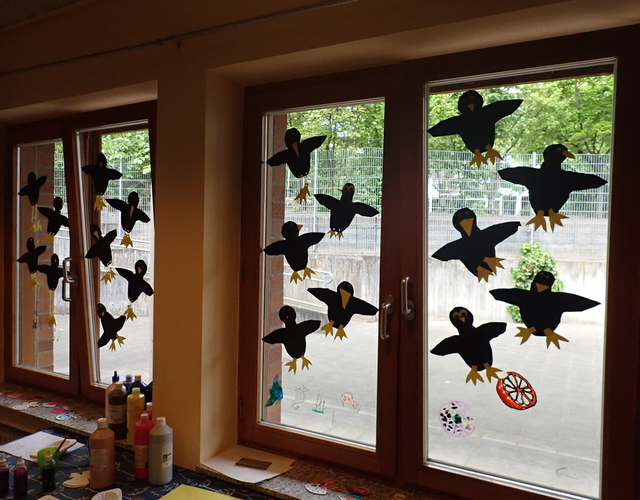 Pinguin-Basteleien schmücken Fenster, Farbtuben stehen auf der Fensterbank.