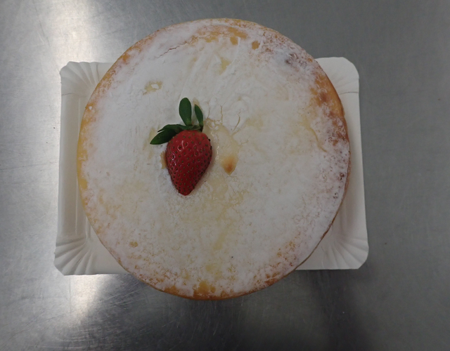 Mit Puderzucker bestäubter Kuchen mit einer Erdbeere auf weißem Teller.