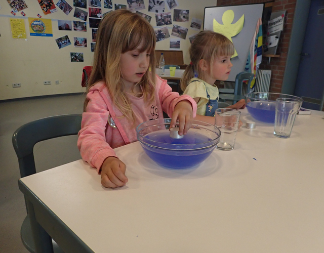 Mädchen stellt Kerze in Schüssel mit blauem Wasser beim Experiment.