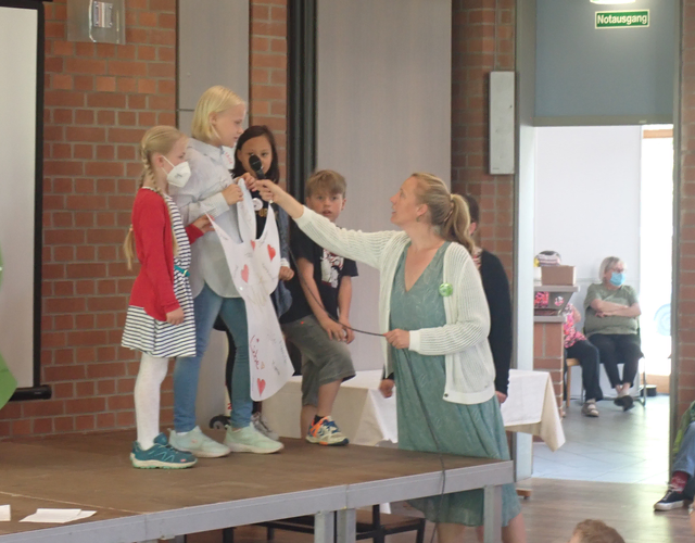 Kinder präsentieren auf der Bühne, Frau hält ihnen das Mikrofon hin.