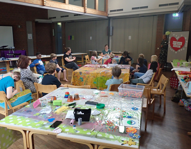 Kinder und Erwachsene sitzen im Kreativraum mit sichtbarem Bastelmaterial.