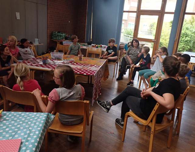Kinder und Erwachsene sitzen im Kreis und unterhalten sich im Klassenraum.