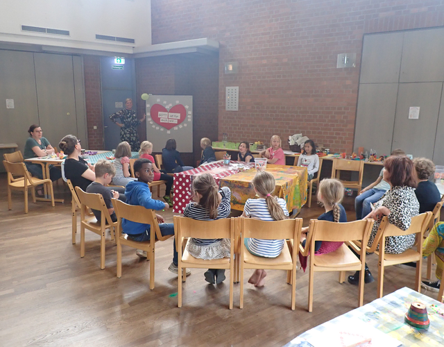 Kinder und Erwachsene sitzen an Tischen in einem Gemeindesaal, schauen Präsentation.