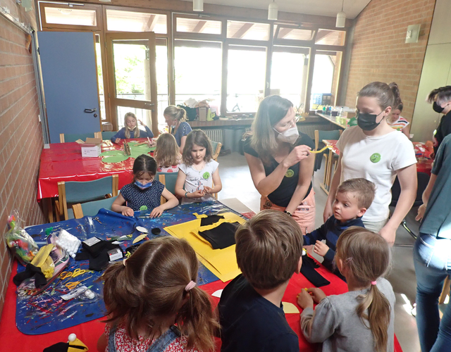Kinder und Erwachsene basteln gemeinsam an langen Tischen mit buntem Material.